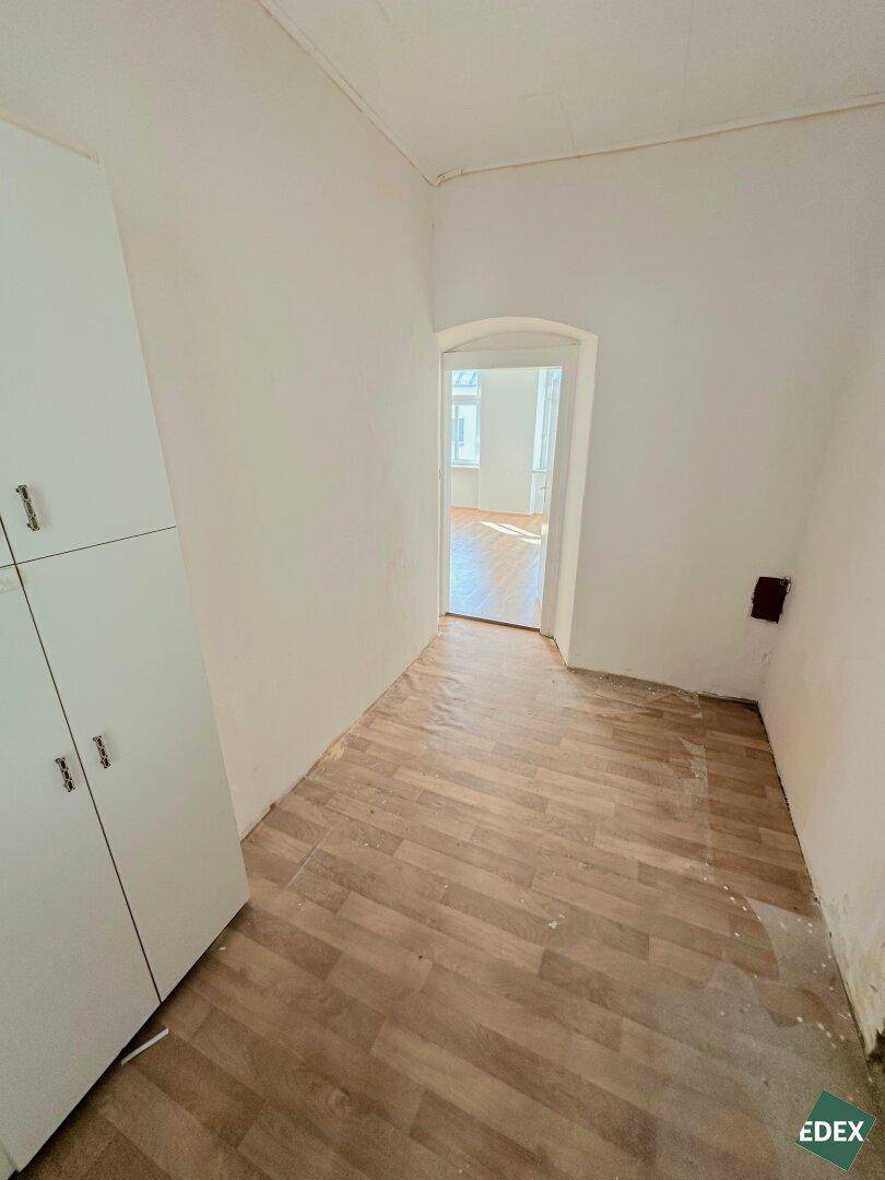 Schmaler Flur mit Laminatboden und einem Schrank, der zu einem hellen Zimmer führt.