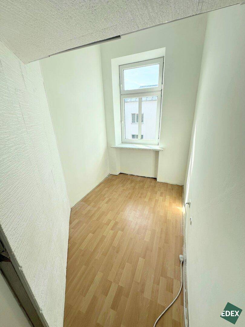Kleiner Raum mit Laminatboden und einem Fenster, ideal als Abstellraum oder Kabinett.