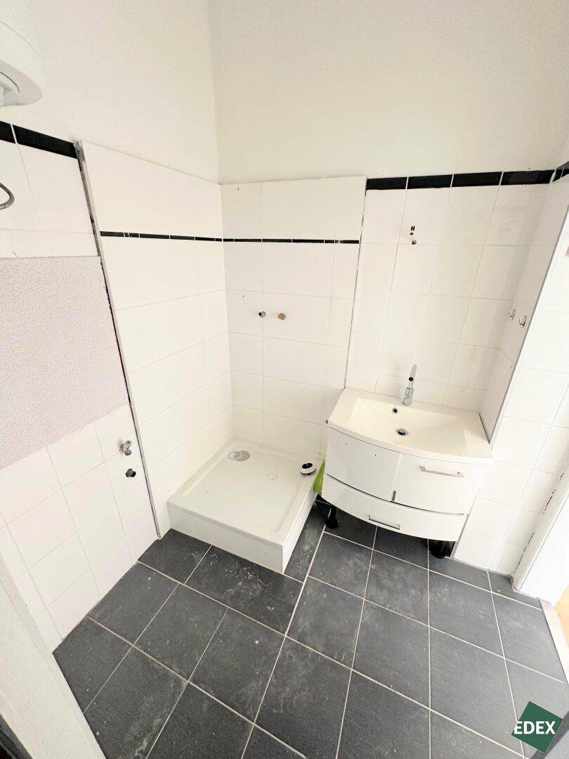 Badezimmer mit Duschbereich, Waschbecken und dunklen Bodenfliesen, funktional und hell.