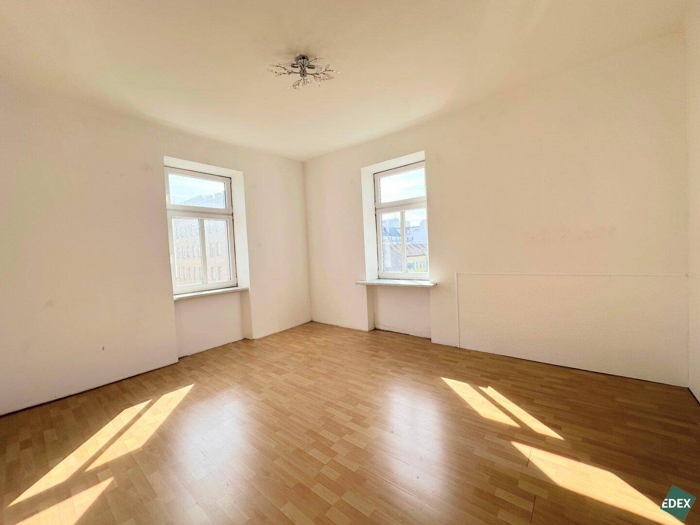 Lichtdurchflutetes Zimmer mit Laminatboden und zwei Fenstern, bereit zur individuellen Gestaltung.