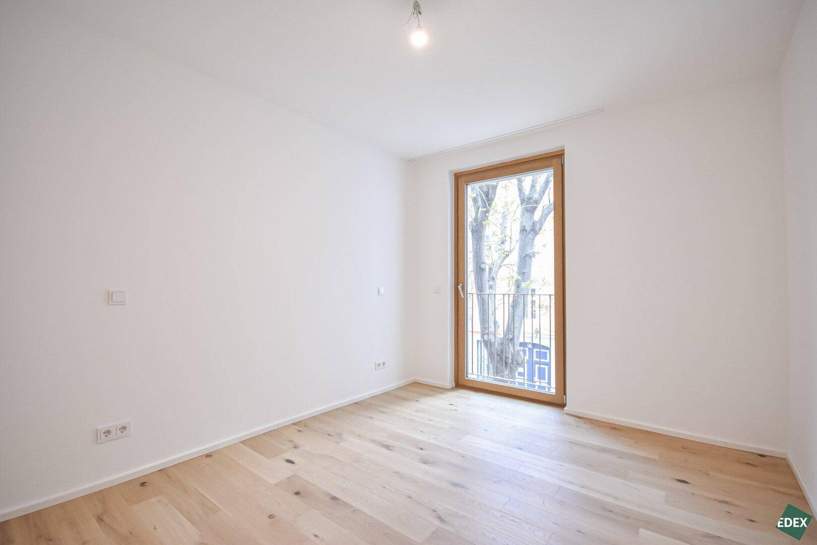 Helles Schlafzimmer mit Holzboden und Zugang zu einem französischen Balkon.