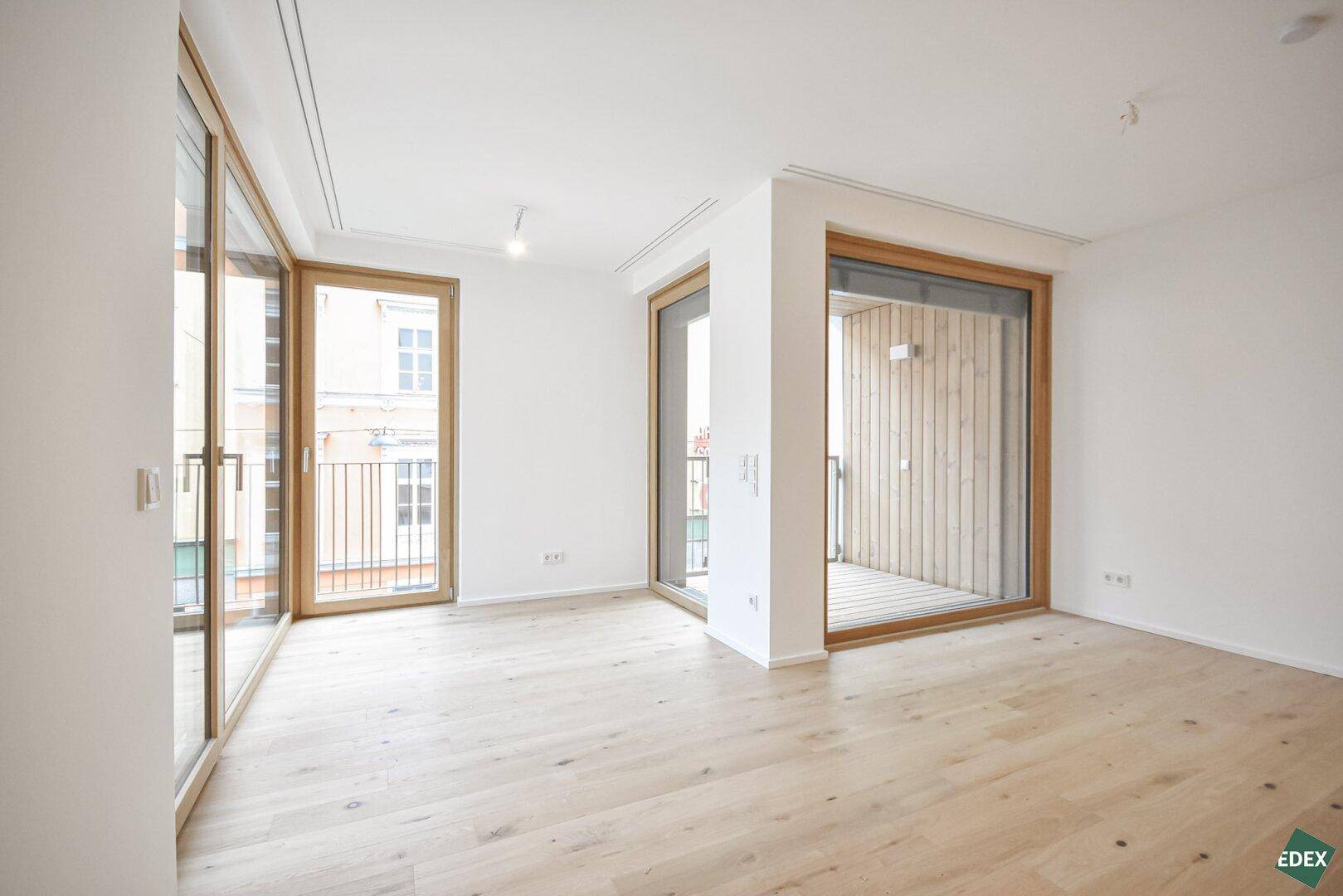 Geräumiges, helles Wohnzimmer mit Holzboden und mehreren Fenstern, die viel Licht hereinlassen.