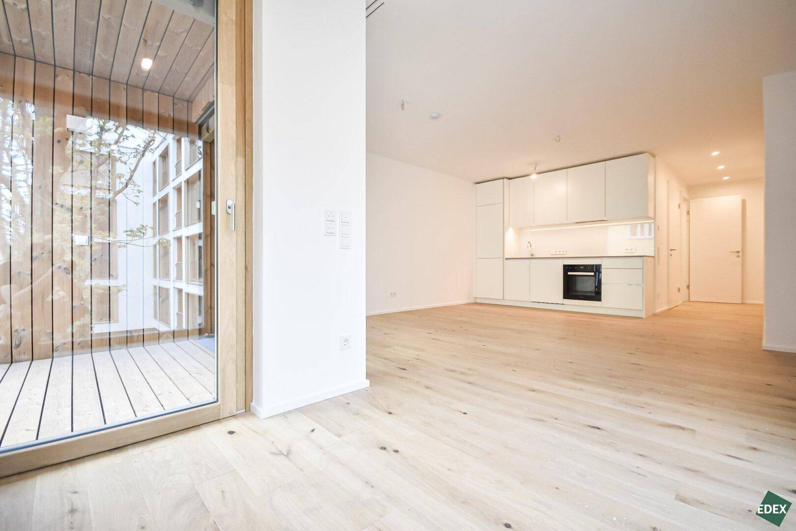 Offener Wohnbereich mit integrierter Küchenzeile und Zugang zu einem Balkon.
