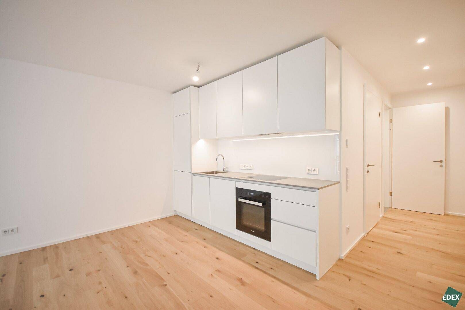 Moderne, kompakte Küchenzeile in Weiß mit integrierten Geräten und heller Arbeitsplatte.