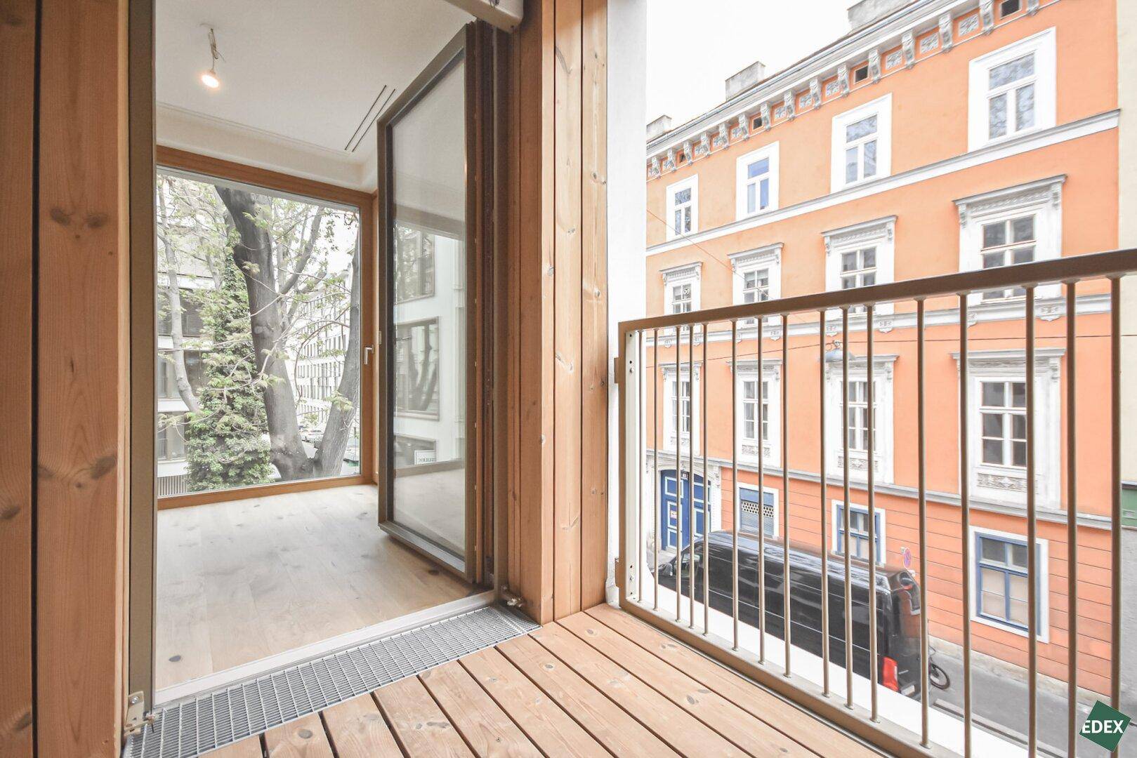 Kleiner Holzbalkon mit Blick auf die Straße und gegenüberliegende Gebäude.