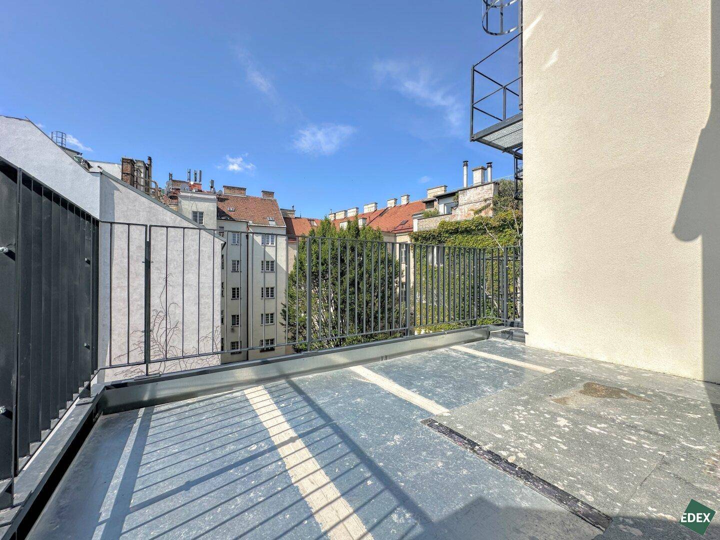 Kleiner Balkon mit Metallgeländer und Blick auf die umliegenden Gebäude und Bäume.