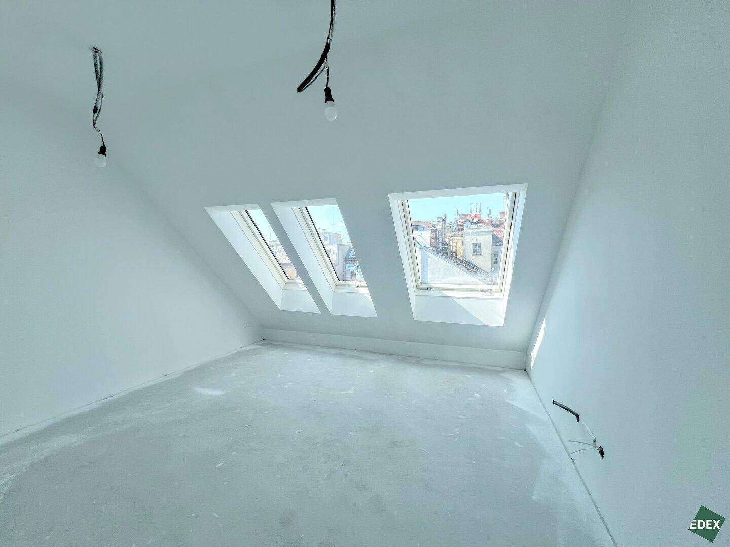 Rohbau im Dachgeschoss mit kleineren Dachfenstern, die viel Tageslicht hereinlassen.