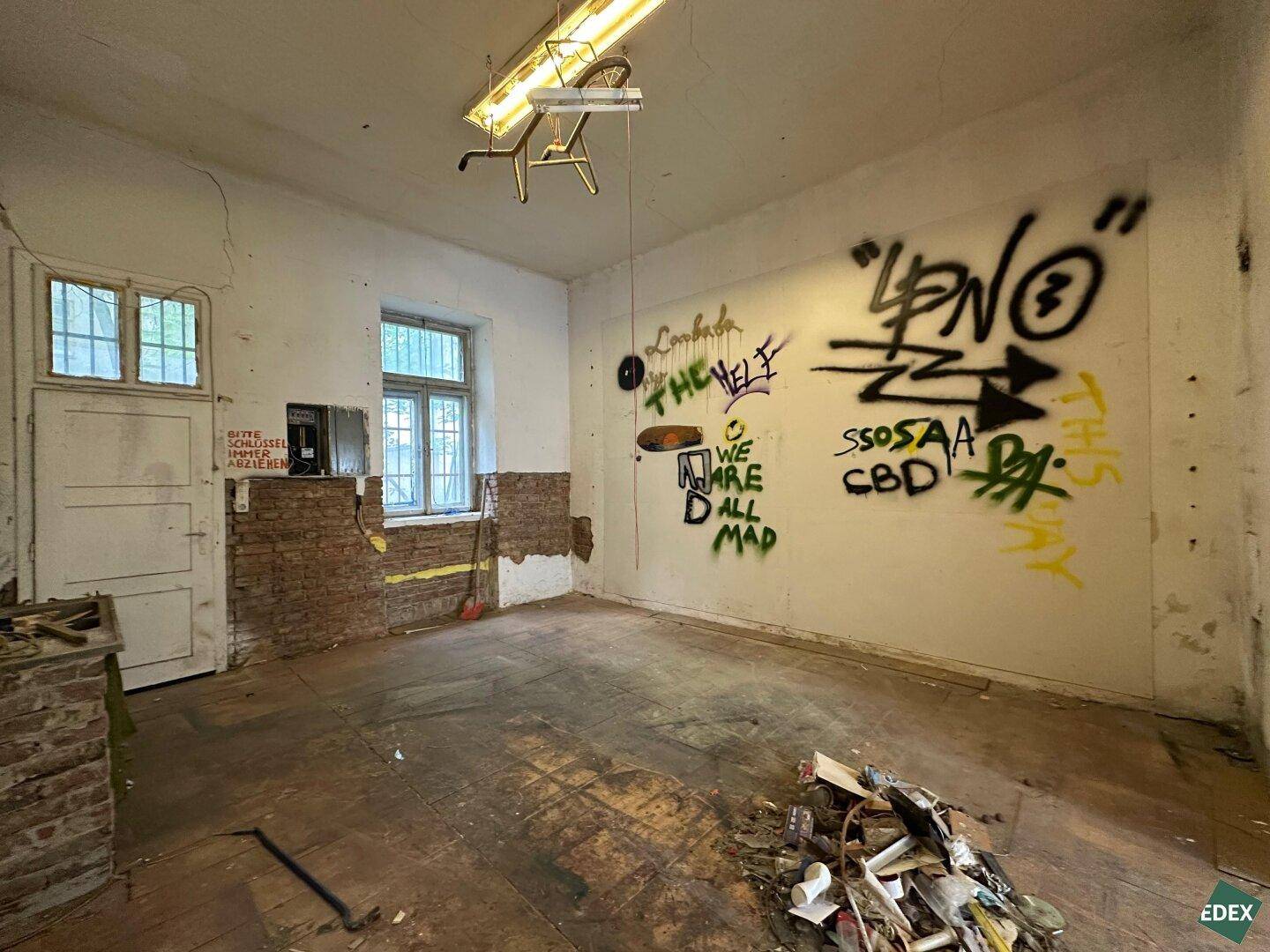 Renovierungsbedürftiger Raum mit Graffiti an der Wand und sichtbaren Gebrauchsspuren.