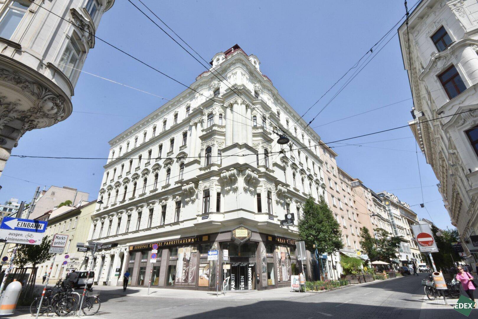 Historisches Eckgebäude in der Stadt mit klassischer Architektur und Geschäften im Erdgeschoss.