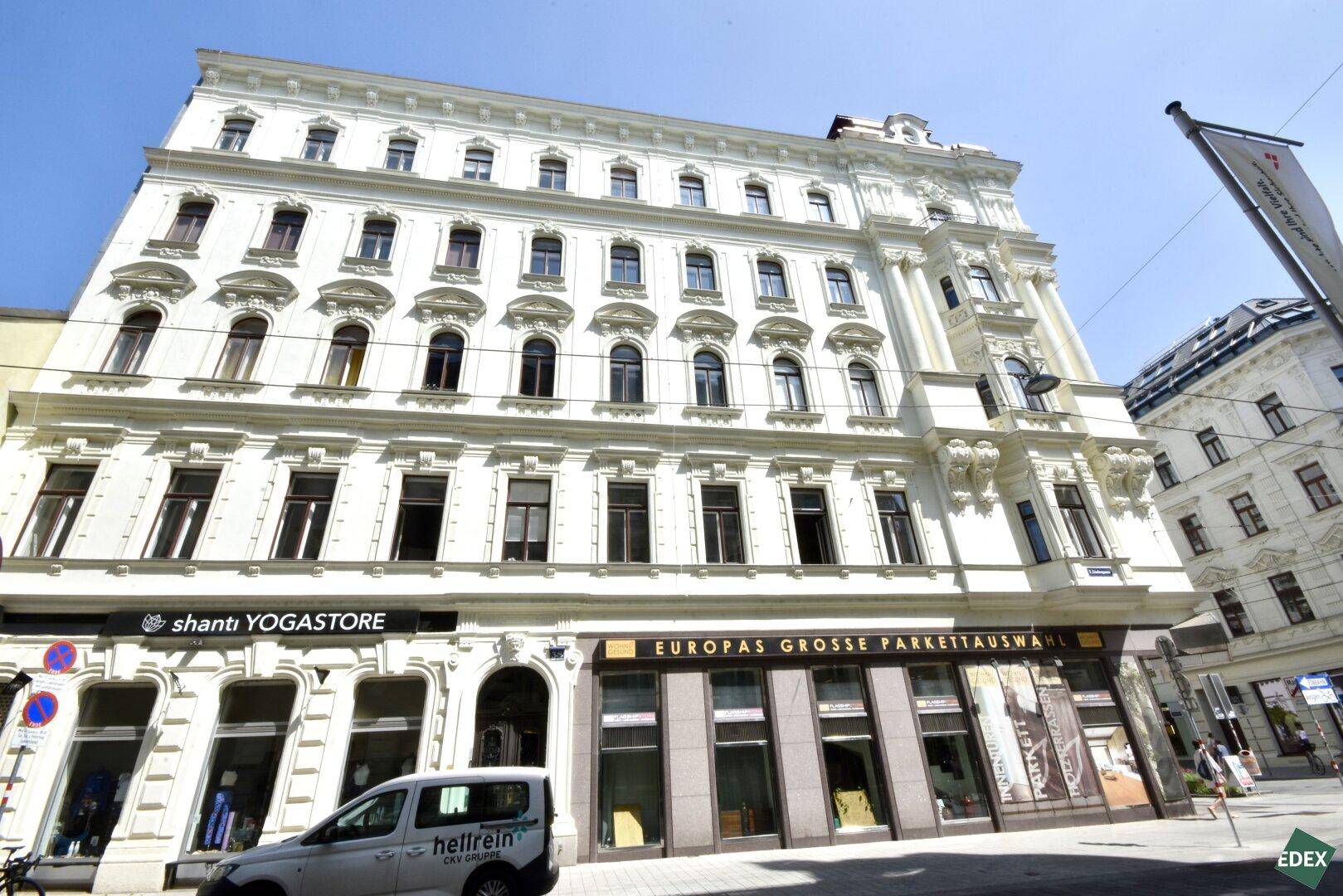 Prächtige Fassade eines Altbaus mit vielen Fenstern und Geschäften im Erdgeschoss.