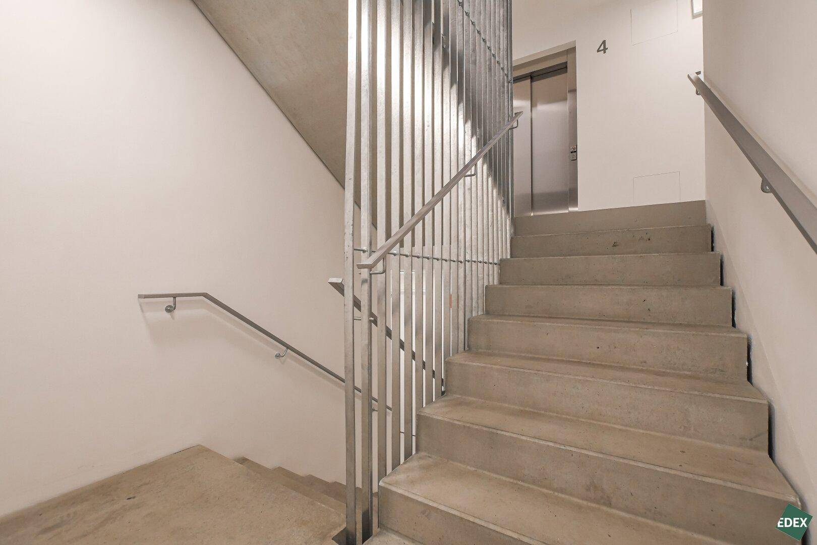 Modernes Treppenhaus mit Betonstufen und Metallgeländer, gut beleuchtet und funktional gestaltet.