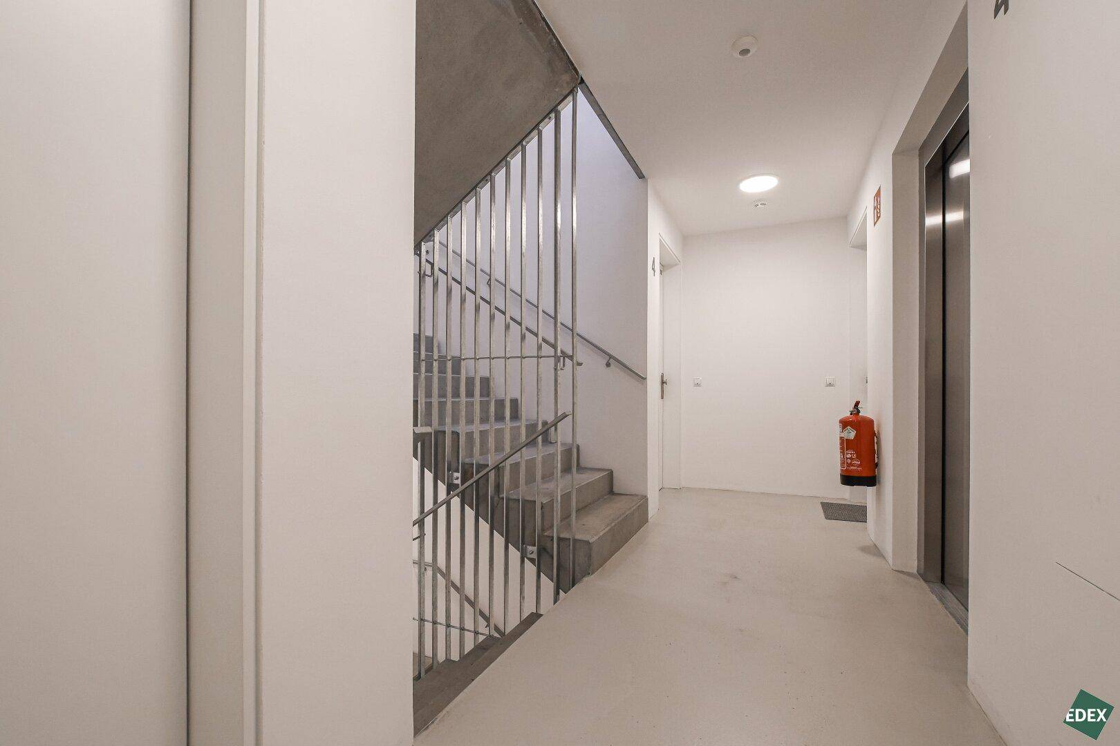 Geräumiger Flur mit Treppenhaus und Aufzug, ausgestattet mit einem Feuerlöscher für die Sicherheit.