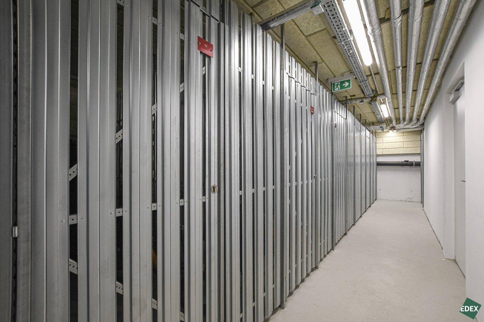 Reihe von Abstellräumen im Kellerbereich mit Metallwänden und Beleuchtung für zusätzlichen Stauraum.