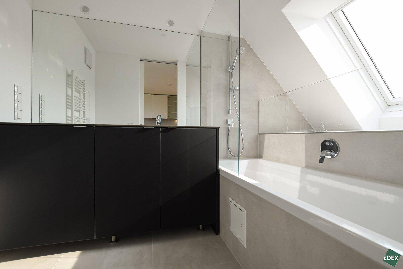 Modernes Badezimmer mit Badewanne, Dusche, großem Spiegel und Dachfenster.