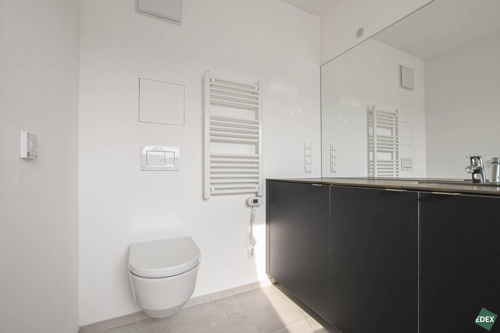 Helles Badezimmer mit wandhängendem WC, beheiztem Handtuchhalter und großem Spiegel.