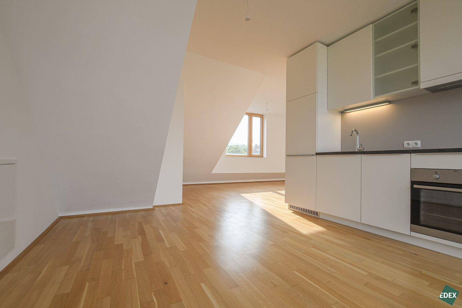 Heller offener Wohnbereich mit integrierter Küche, Dachschrägen und Holzboden.