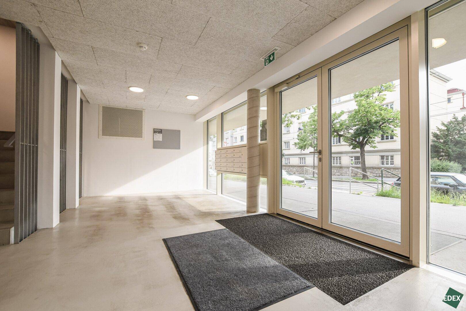 Heller Eingangsbereich des Gebäudes mit großen Glastüren und Briefkästen.