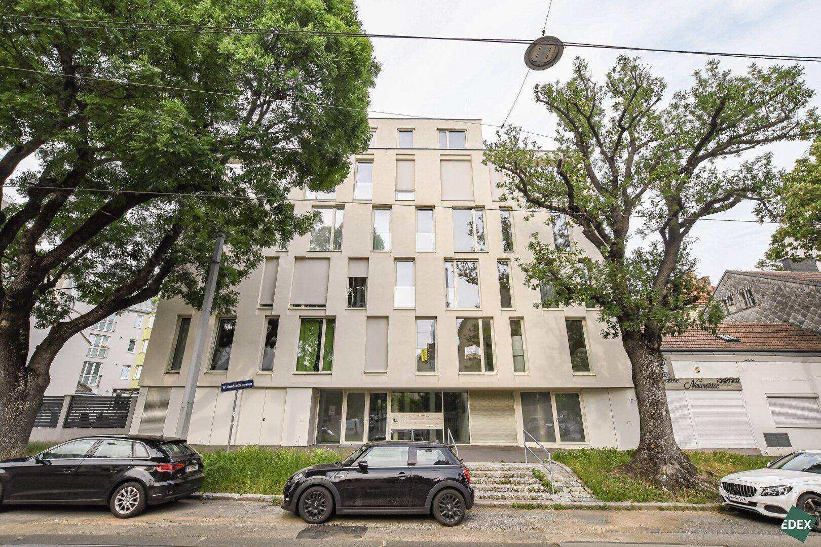 Moderne Wohnfassade mit vielen Fenstern und Bäumen, die das Gebäude umgeben.