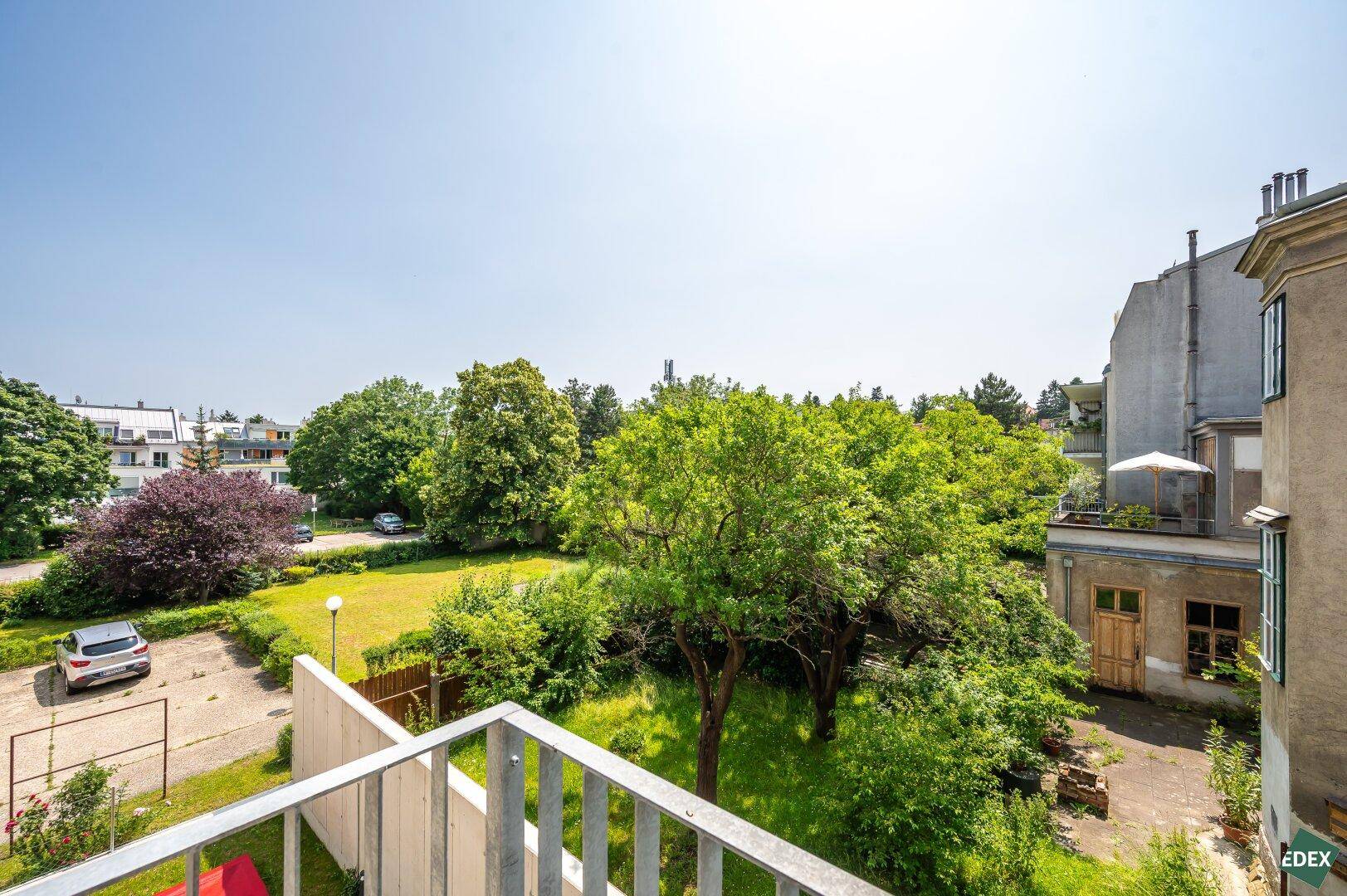 Weitläufiger Blick von einem Balkon auf einen grünen Innenhof mit Bäumen und umliegenden Gebäuden.
