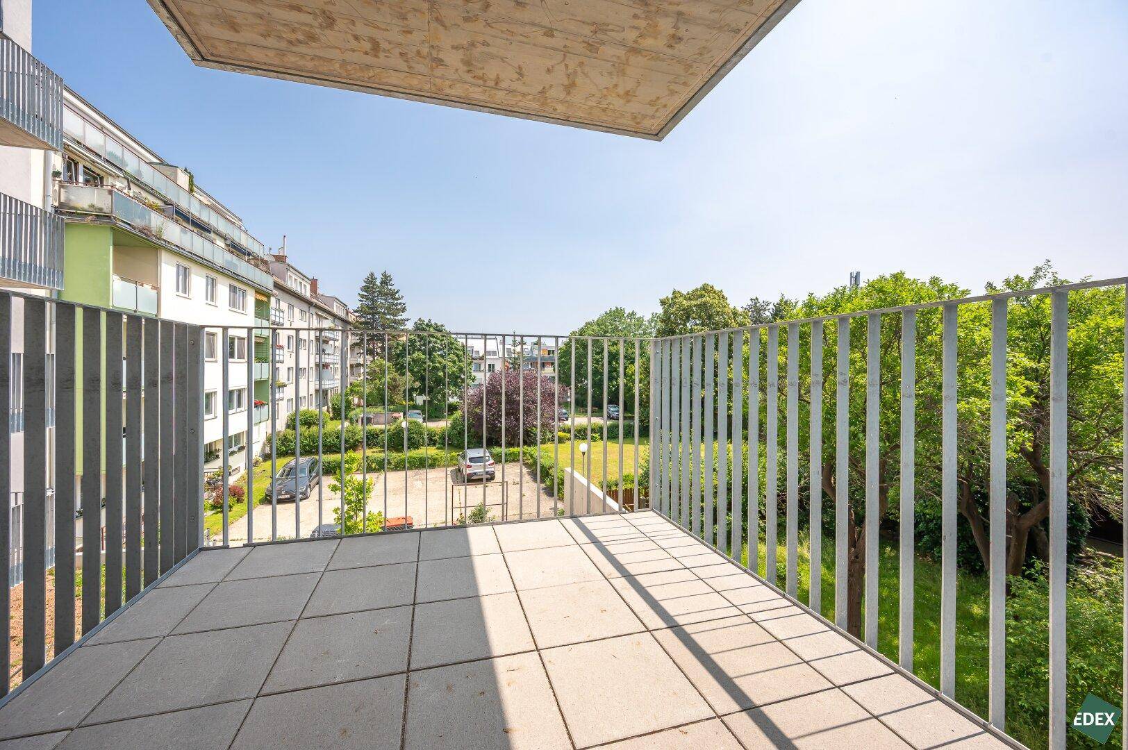Geräumiger Balkon mit Fliesenboden und Metallgeländer, bietet Blick auf einen grünen Innenhof.