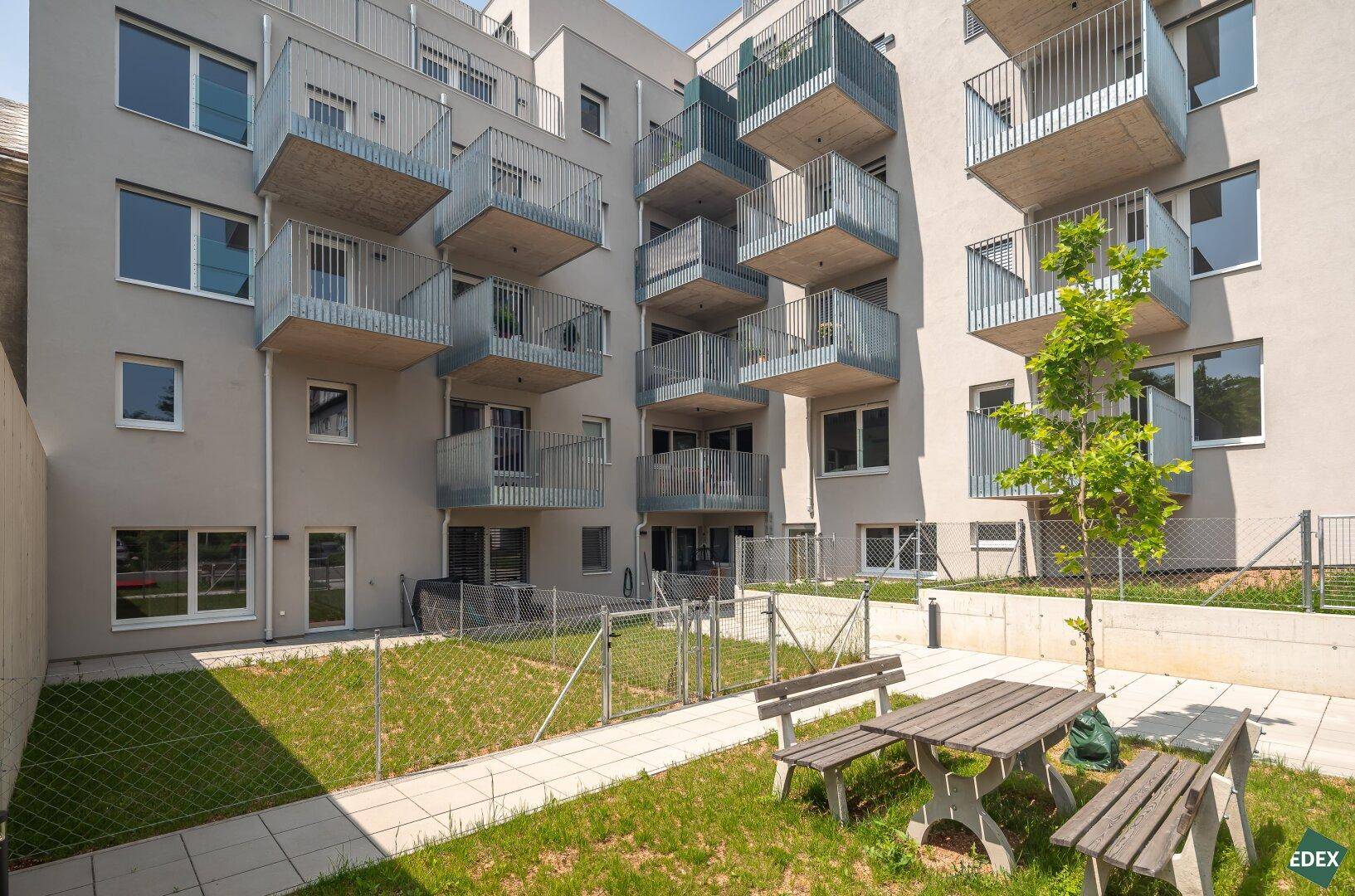 Gemeinschaftsgarten mit Sitzgelegenheiten und Rasenflächen hinter dem Gebäude.