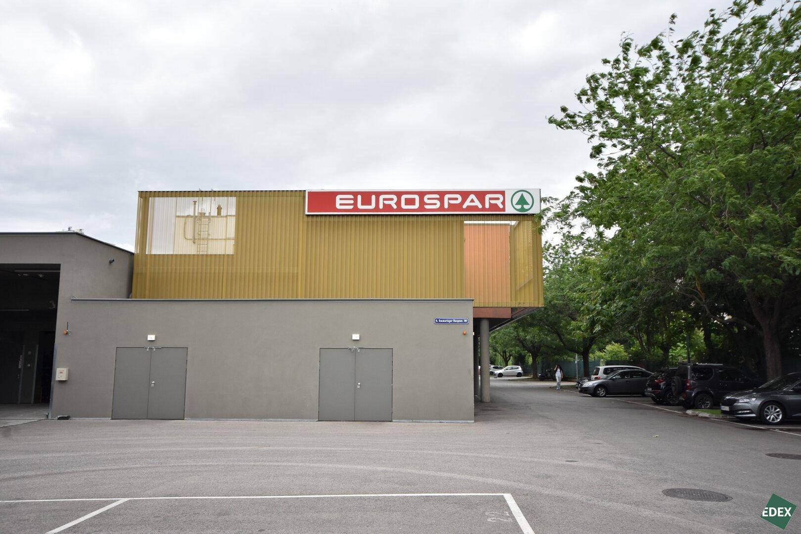 Ansicht des Eurospar-Gebäudes mit seiner markanten gold-grauen Fassade und dem angrenzenden Parkplatz unter bewölktem Himmel.