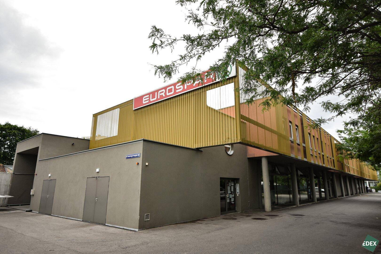 Das Bild zeigt die moderne Fassade eines Eurospar-Gebäudes mit goldfarbenen Akzenten und einem Parkplatzbereich.