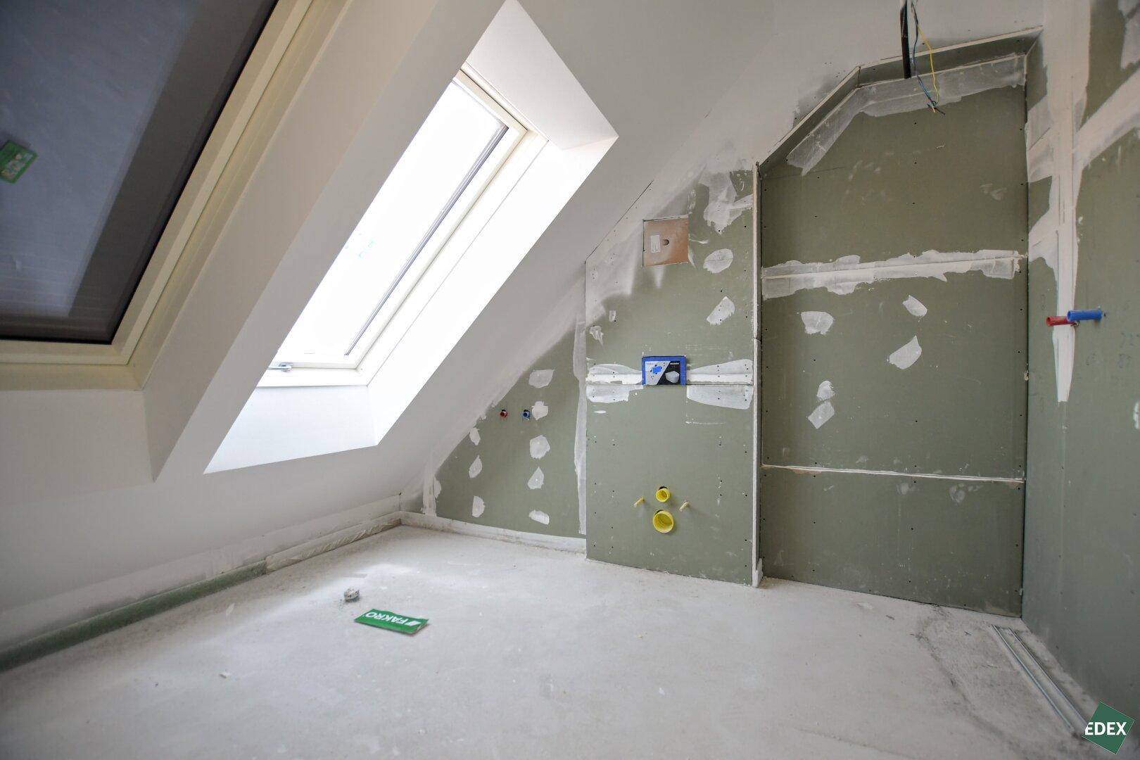 Rohbau eines Badezimmers im Dachgeschoss mit vorbereiteten Anschlüssen und Dachfenster.