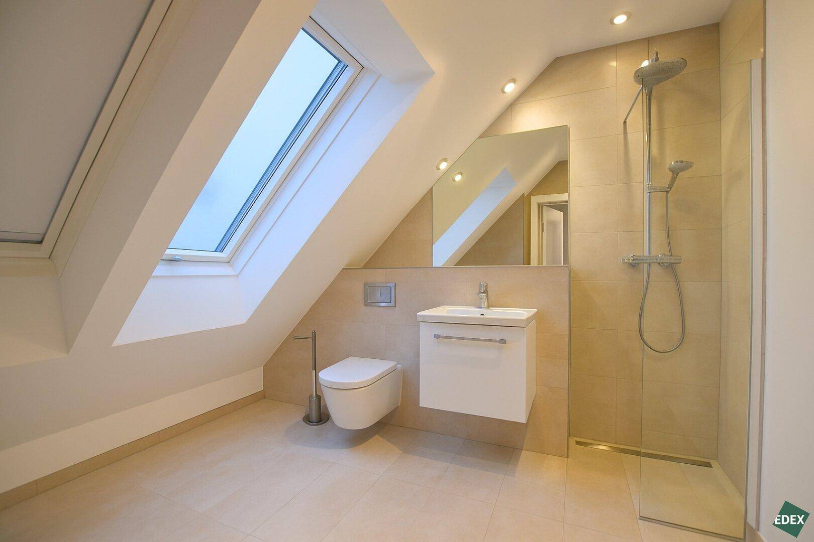 Modernes Badezimmer mit begehbarer Dusche, wandhängendem WC und Dachfenster für natürliches Licht.