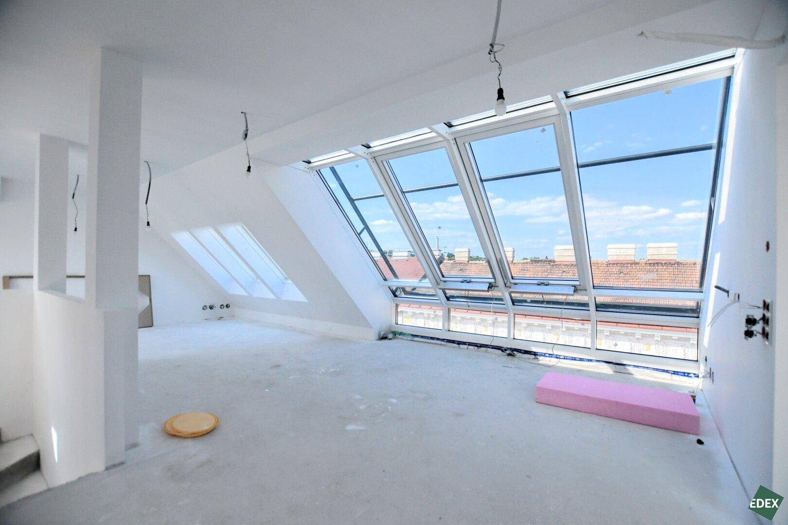 Großer, heller Rohbau im Dachgeschoss mit vielen Dachfenstern und Blick über die Stadt.