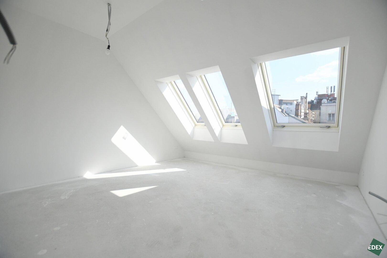 Heller Rohbau im Dachgeschoss mit mehreren Dachfenstern, die viel Sonnenlicht hereinlassen.