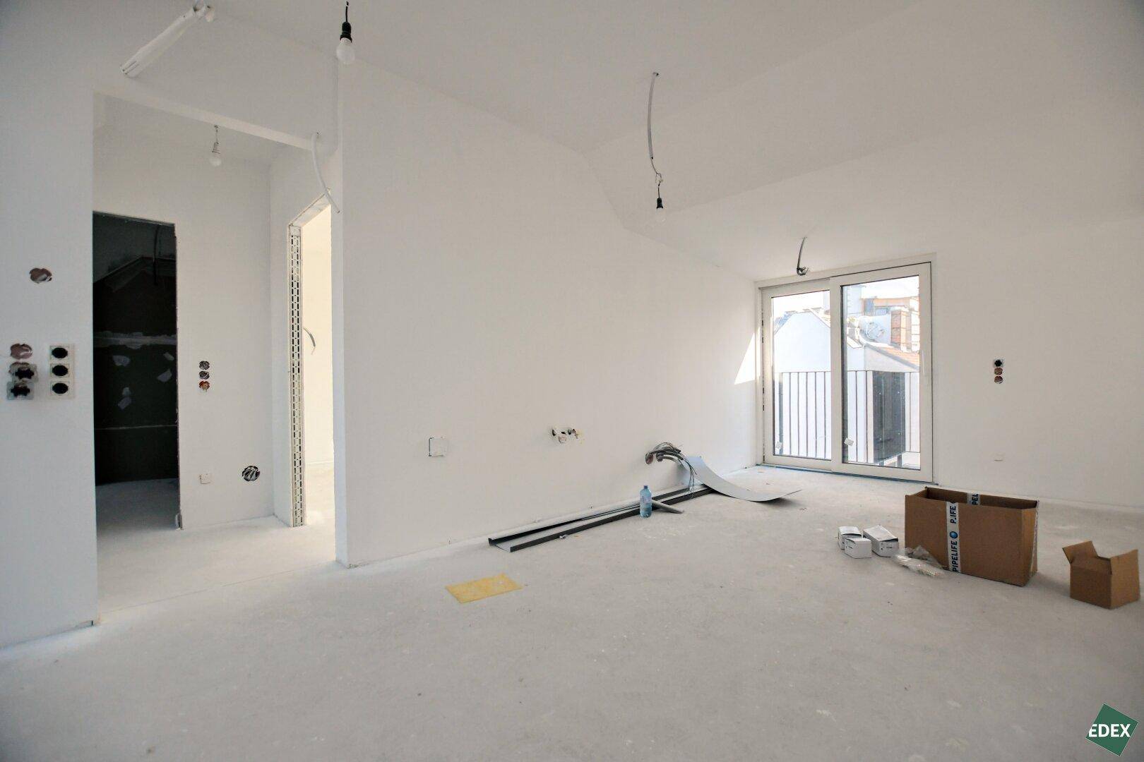 Rohbau im Dachgeschoss mit Zugang zu einem Außenbereich und vorbereiteten Installationen.