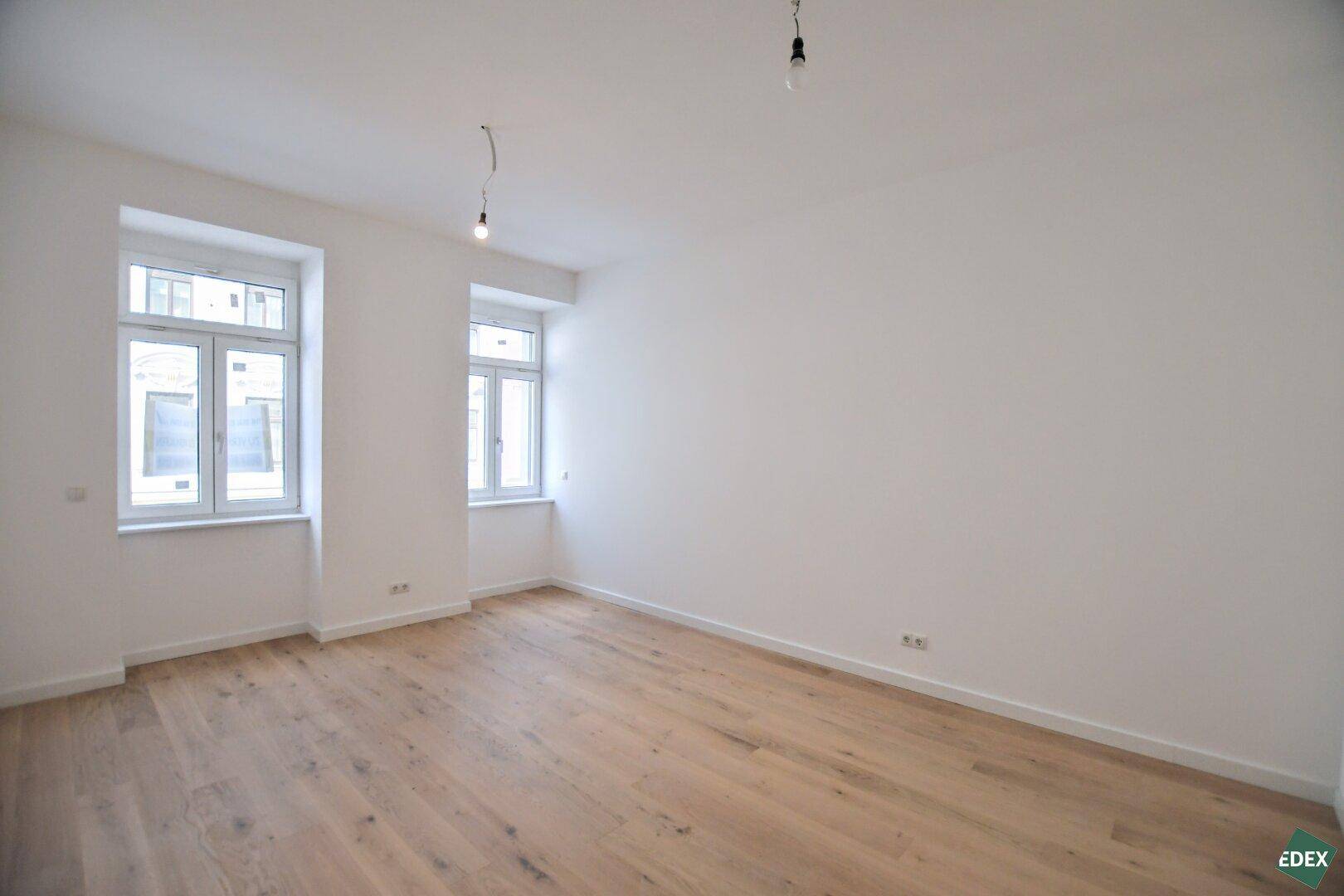 Geräumiger, leerer Raum mit zwei Fenstern und Holzboden, bietet vielseitige Nutzungsmöglichkeiten.