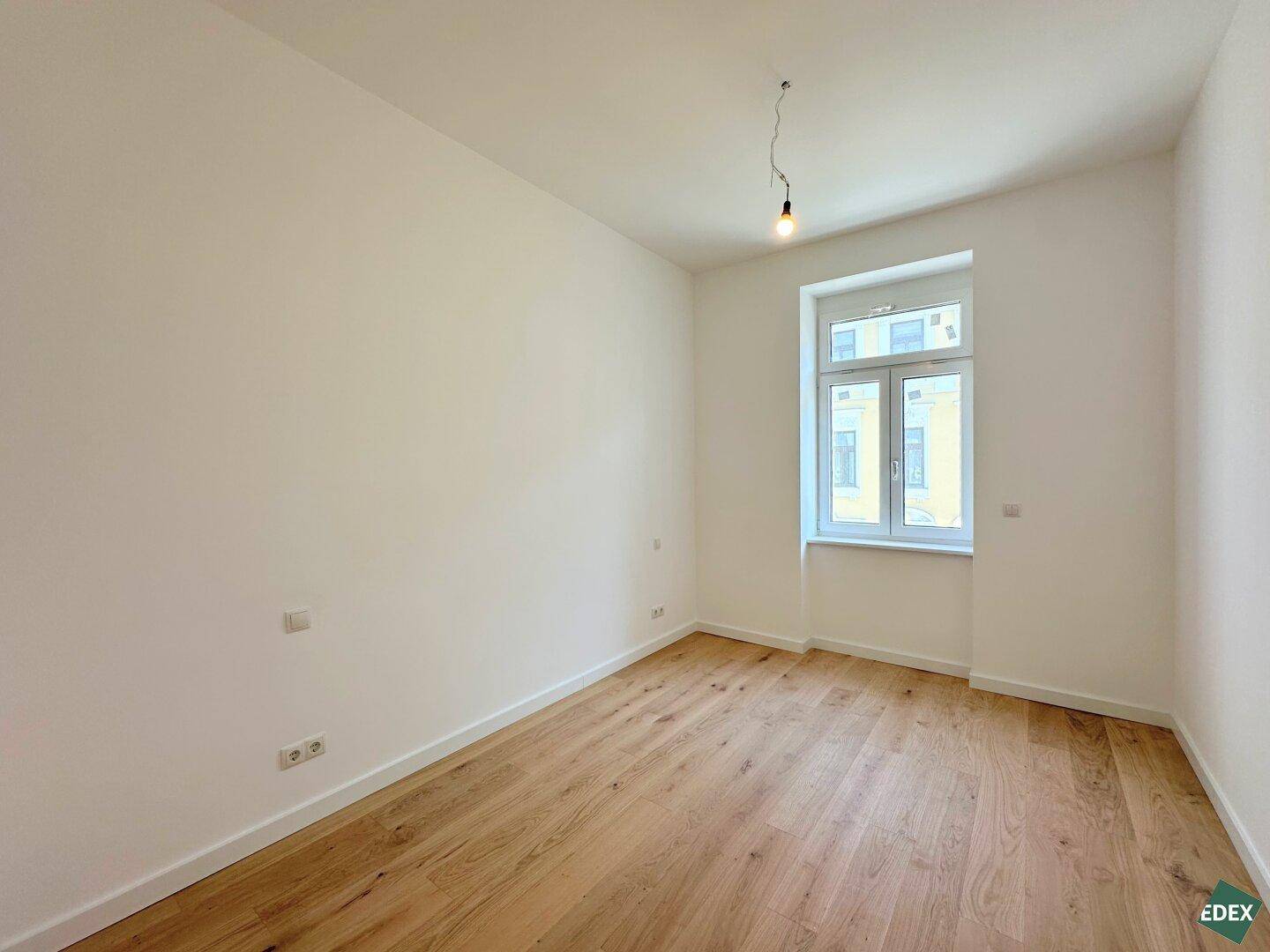 Leerer Raum mit Holzboden und einem großen Fenster, bereit zur individuellen Gestaltung.