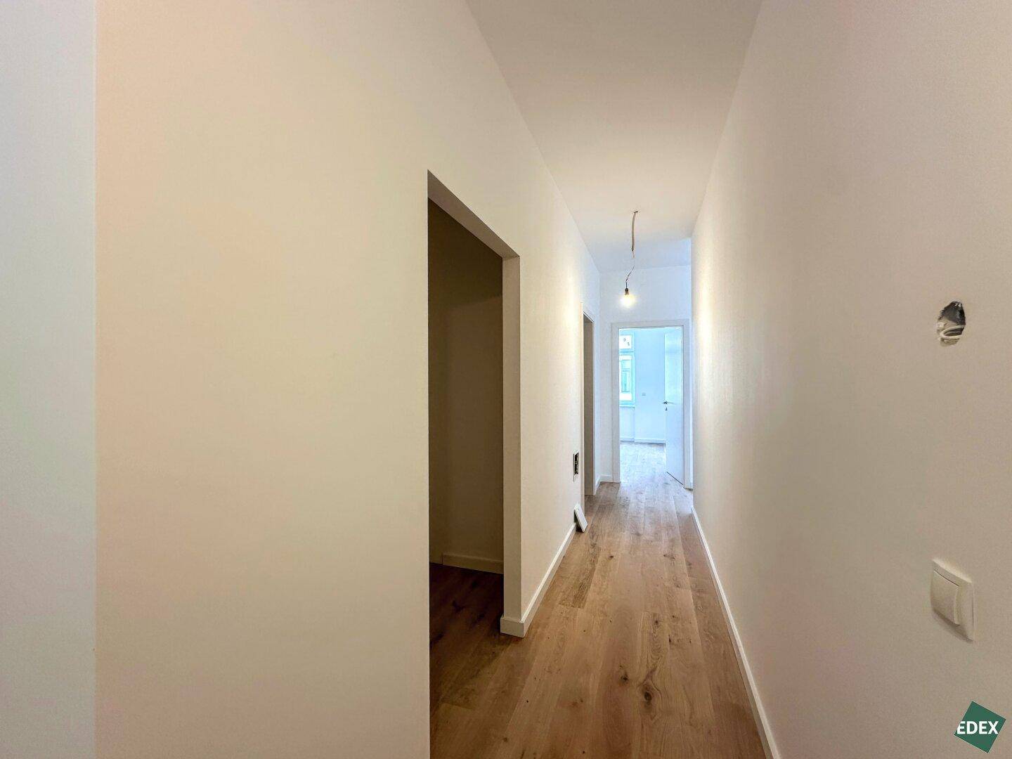 Langer, heller Flur mit Holzboden, der zu weiteren Räumen der Wohnung führt.