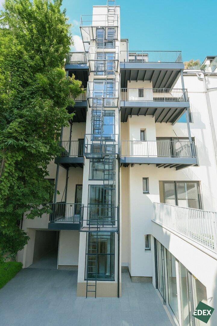 Moderne Gebäudefassade mit externem Glasaufzug und mehreren Balkonen.
