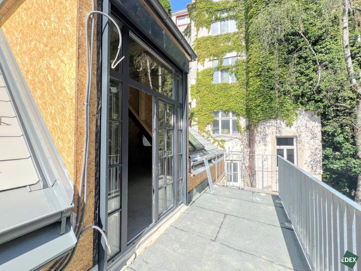 Im Bau befindlicher Balkon mit Blick auf eine begrünte Fassade und umliegende Gebäude.