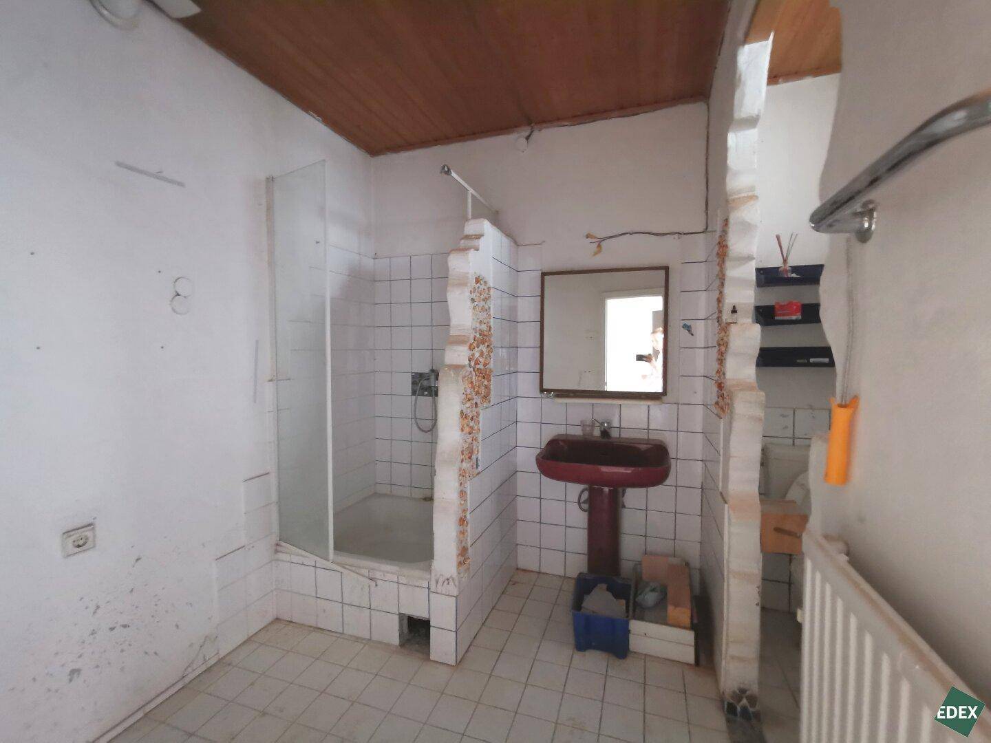 Badezimmer mit Duschbereich, Waschbecken und gefliesten Wänden, das eine Modernisierung erfordert.