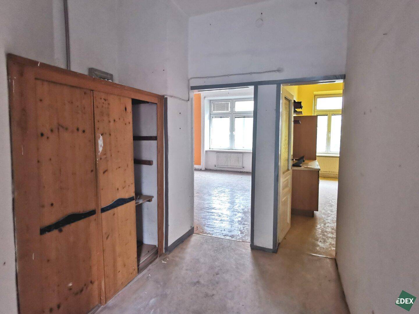 Flur mit eingebautem Holzschrank und Blick in angrenzende, renovierungsbedürftige Räume.