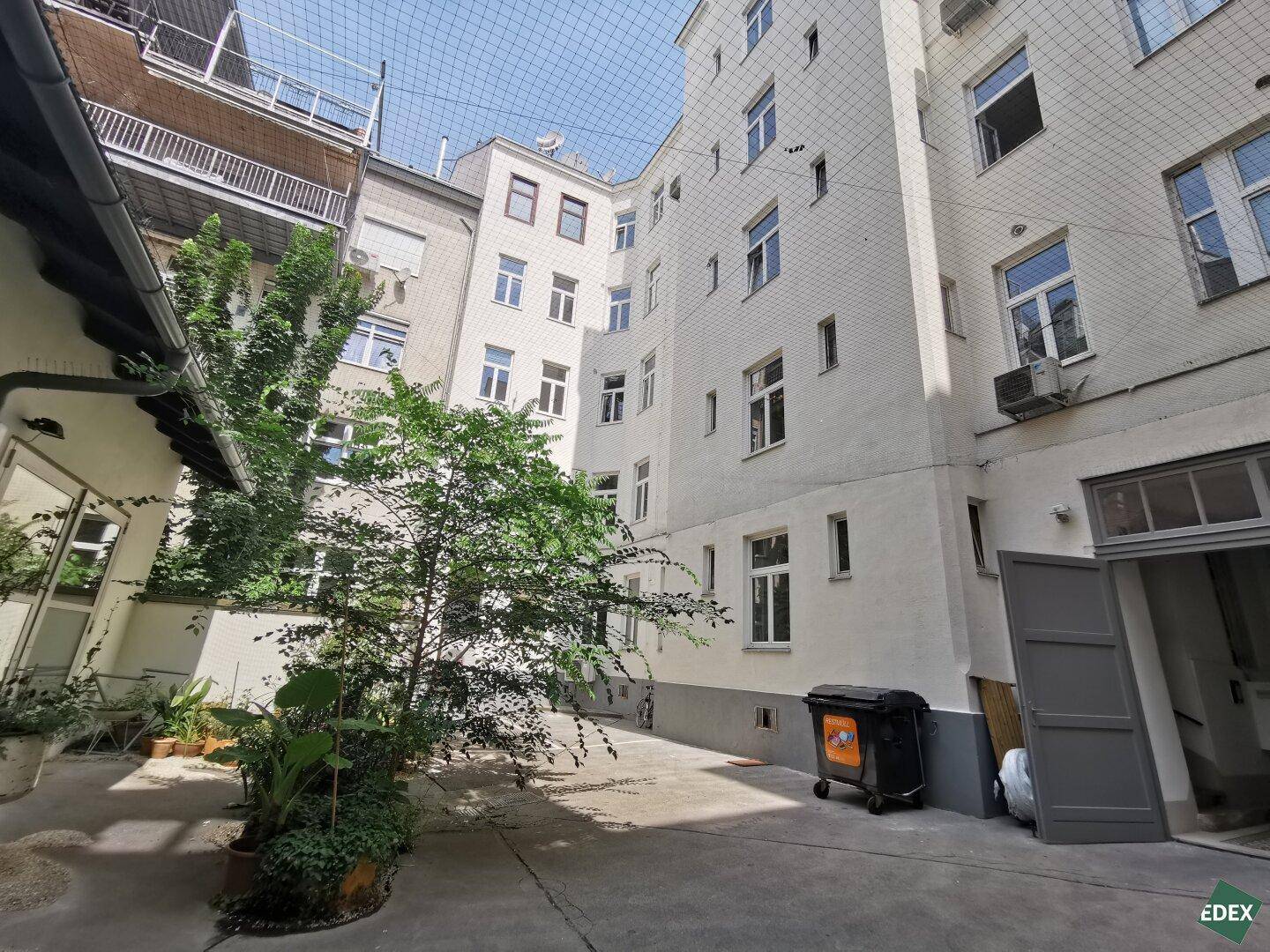 Innenhof eines Wohnkomplexes mit begrünten Bereichen, umgeben von Gebäudefassaden und einem Schutznetz.