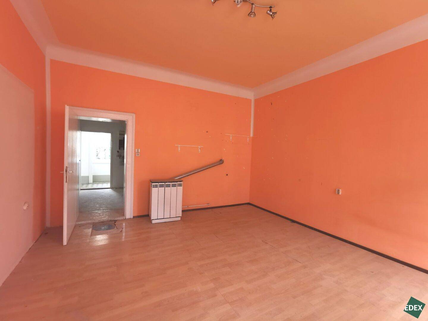 Geräumiges Wohnzimmer mit orangefarbenen Wänden, Holzboden und Zugang zu weiteren Räumen.