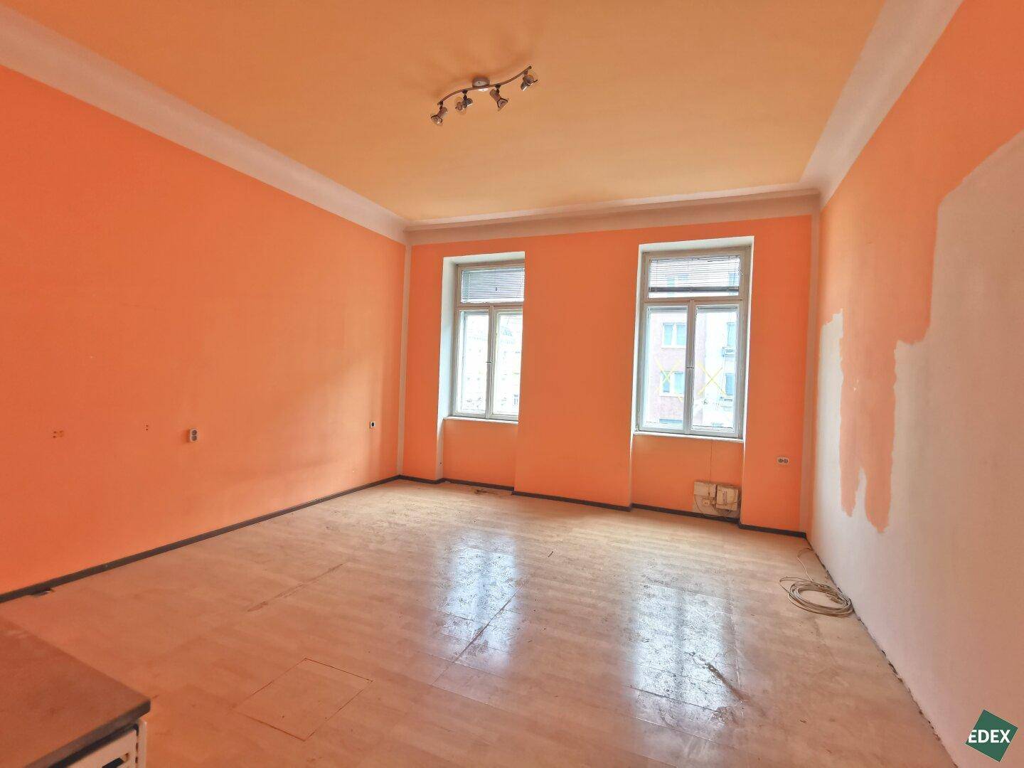 Helles Wohnzimmer mit orangefarbenen Wänden und Holzboden, bereit zur Renovierung.
