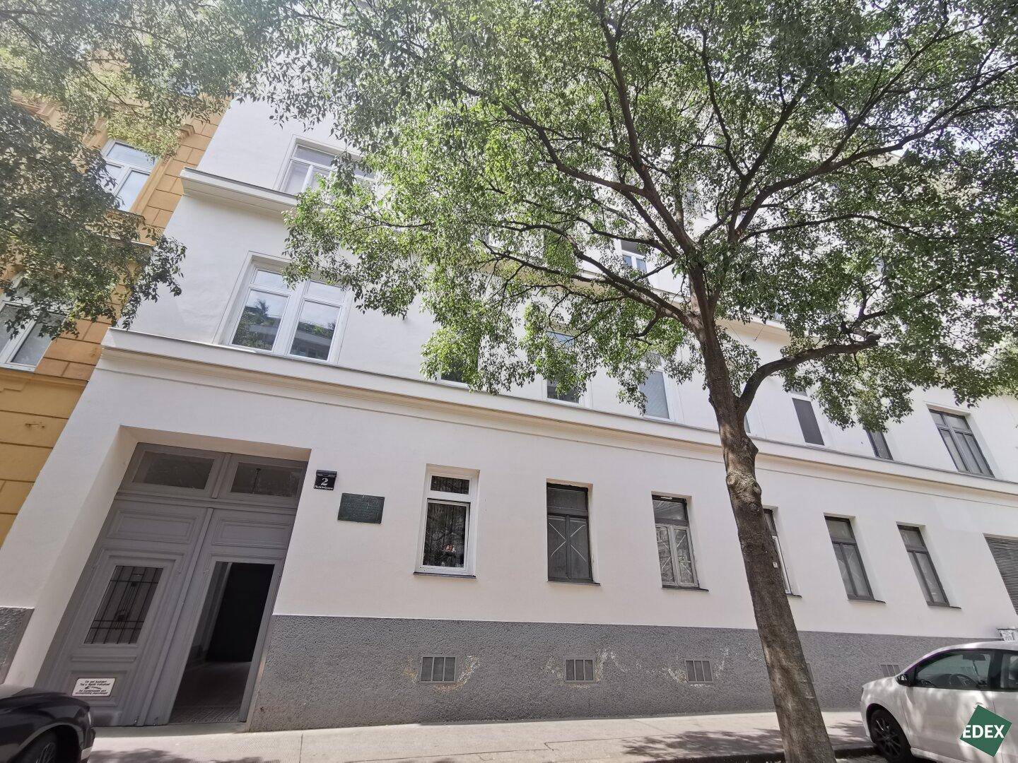 Fassade eines Wohnhauses mit klassischer Architektur und einem großen Baum davor.