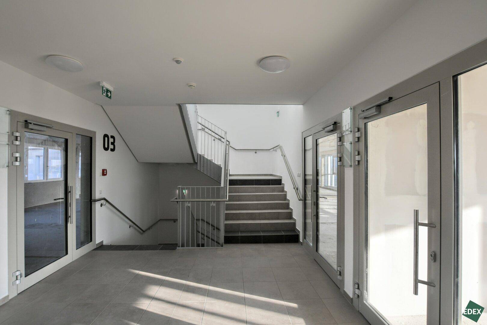 Helles Treppenhaus mit modernen Fliesen, weißen Wänden und einem Geländer aus Metall.