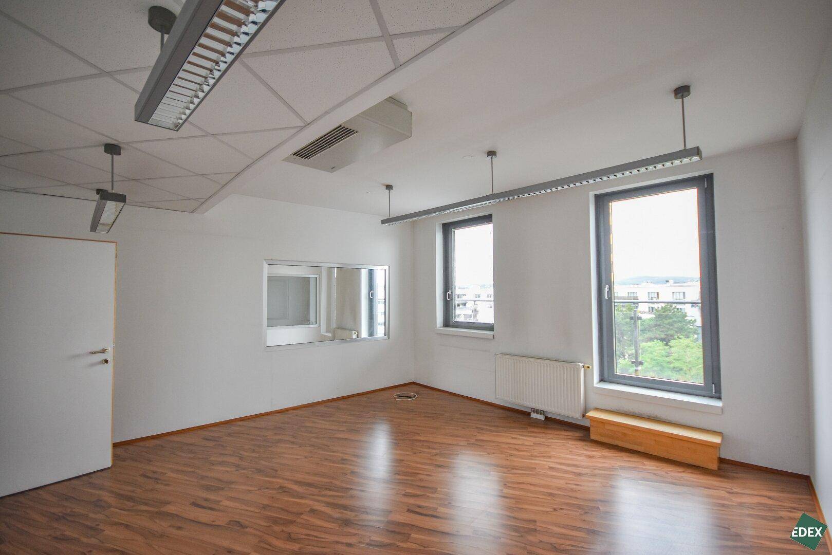 Helles Büro mit Laminatboden, großen Fenstern und einer internen Glaswand.