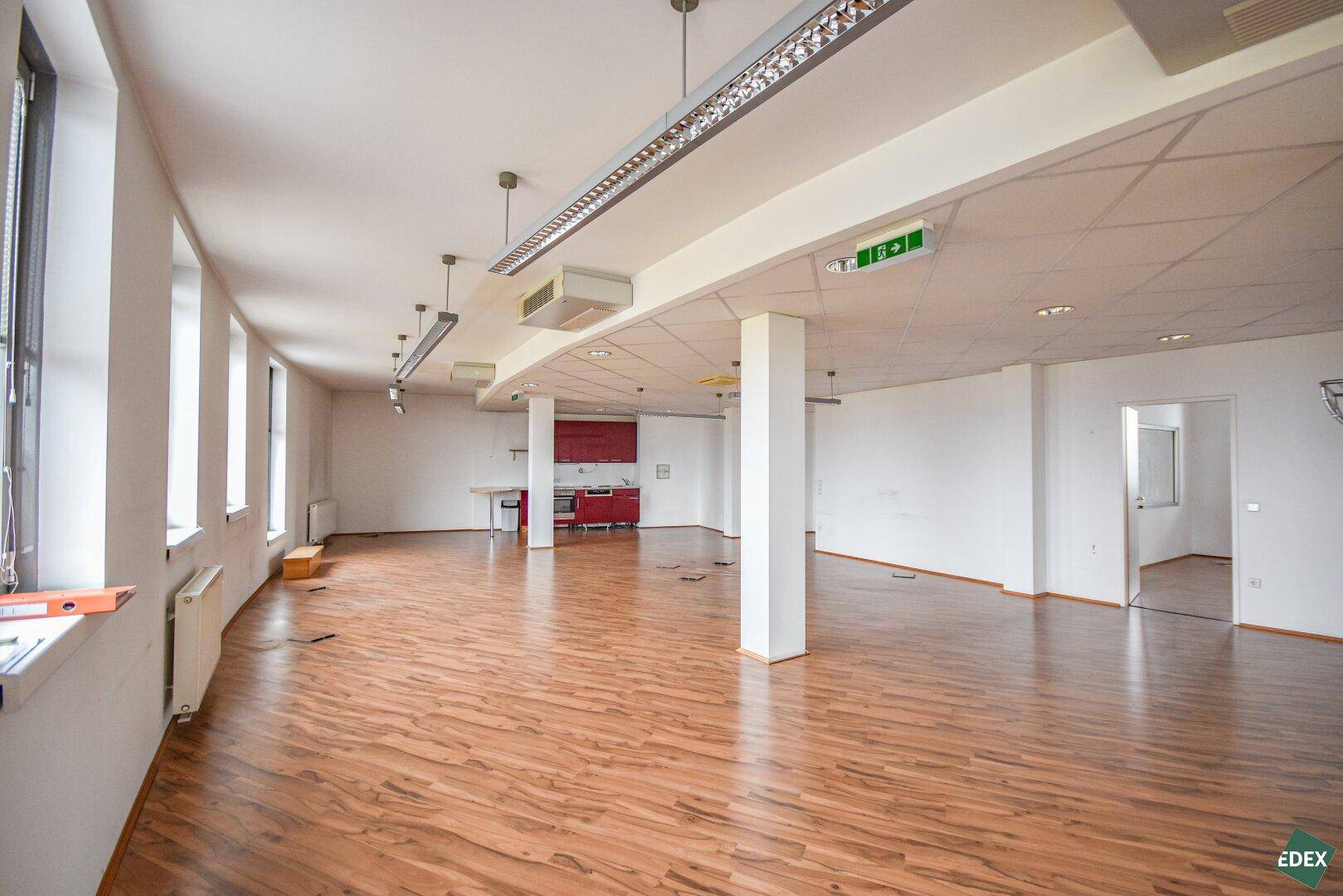 Großes, offenes Büro mit Laminatboden, Säulen und einer integrierten Küchenzeile.