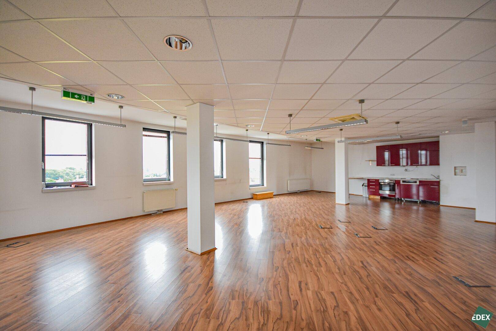 Weitläufiges, offenes Büro mit Laminatboden, mehreren Fenstern und einer roten Küchenzeile.