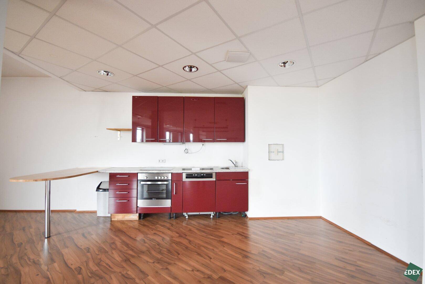 Moderne Küchenzeile in Rot mit integrierten Geräten und einer kleinen Theke.