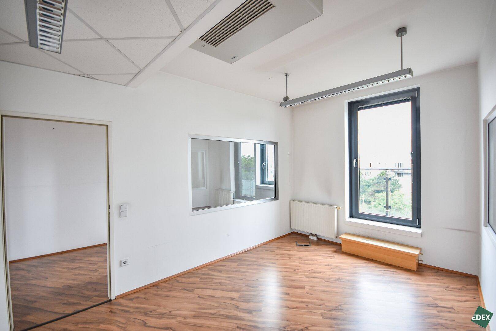 Helles Büro mit Laminatboden, großen Fenstern und einer internen Glaswand.