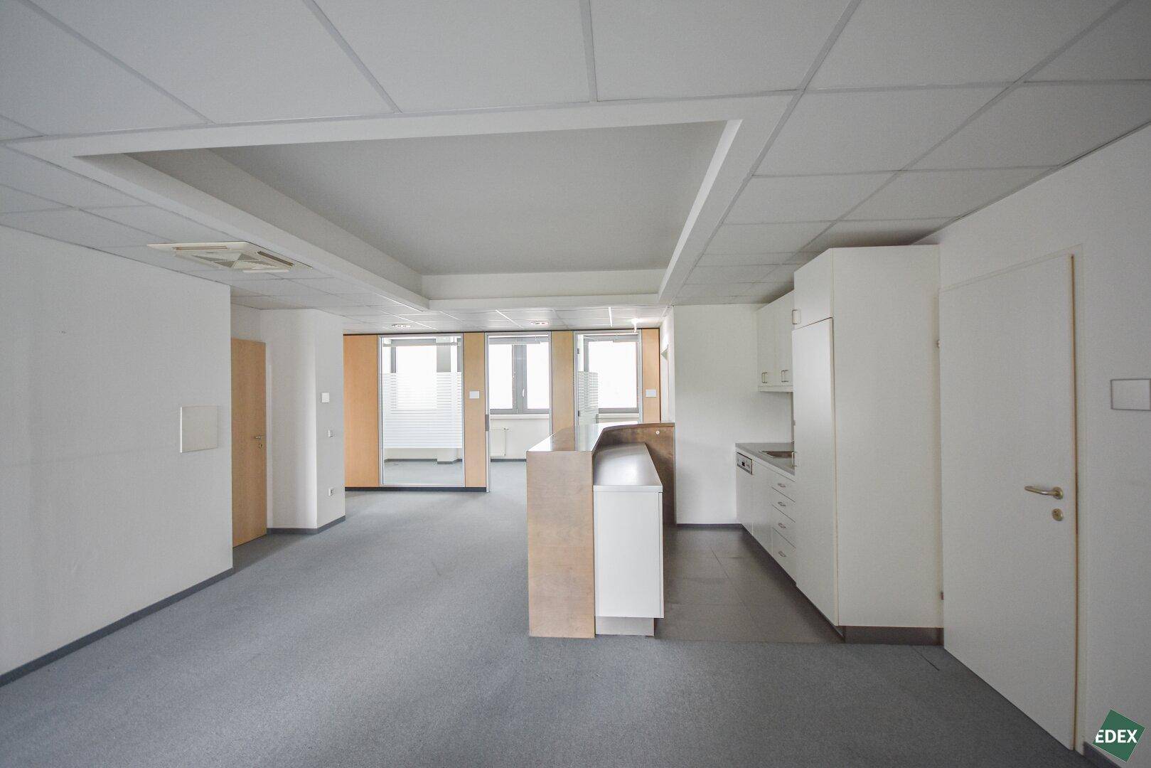 Großes Büro mit integrierter Küchenzeile und Blick auf die Fensterfront.